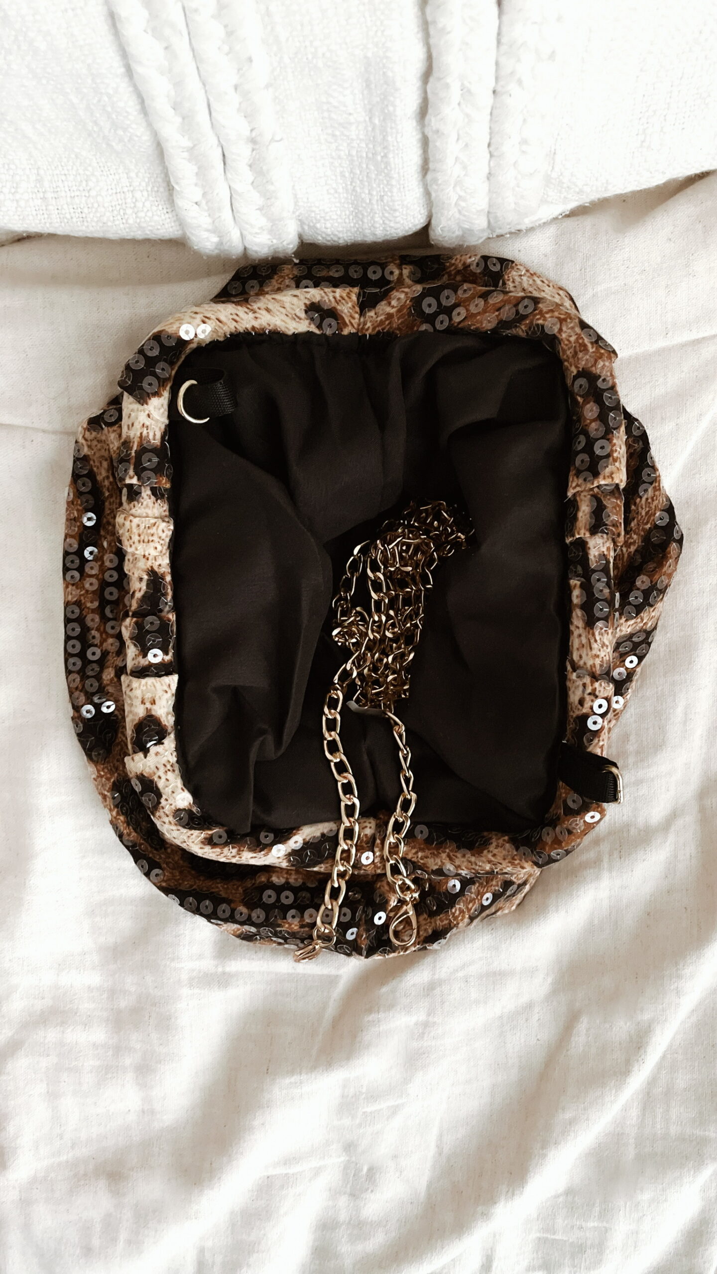 Femme tenant un sac à sequins léopard scintillant, assorti à une tenue brune élégante avec chemisier et blazer en laine.