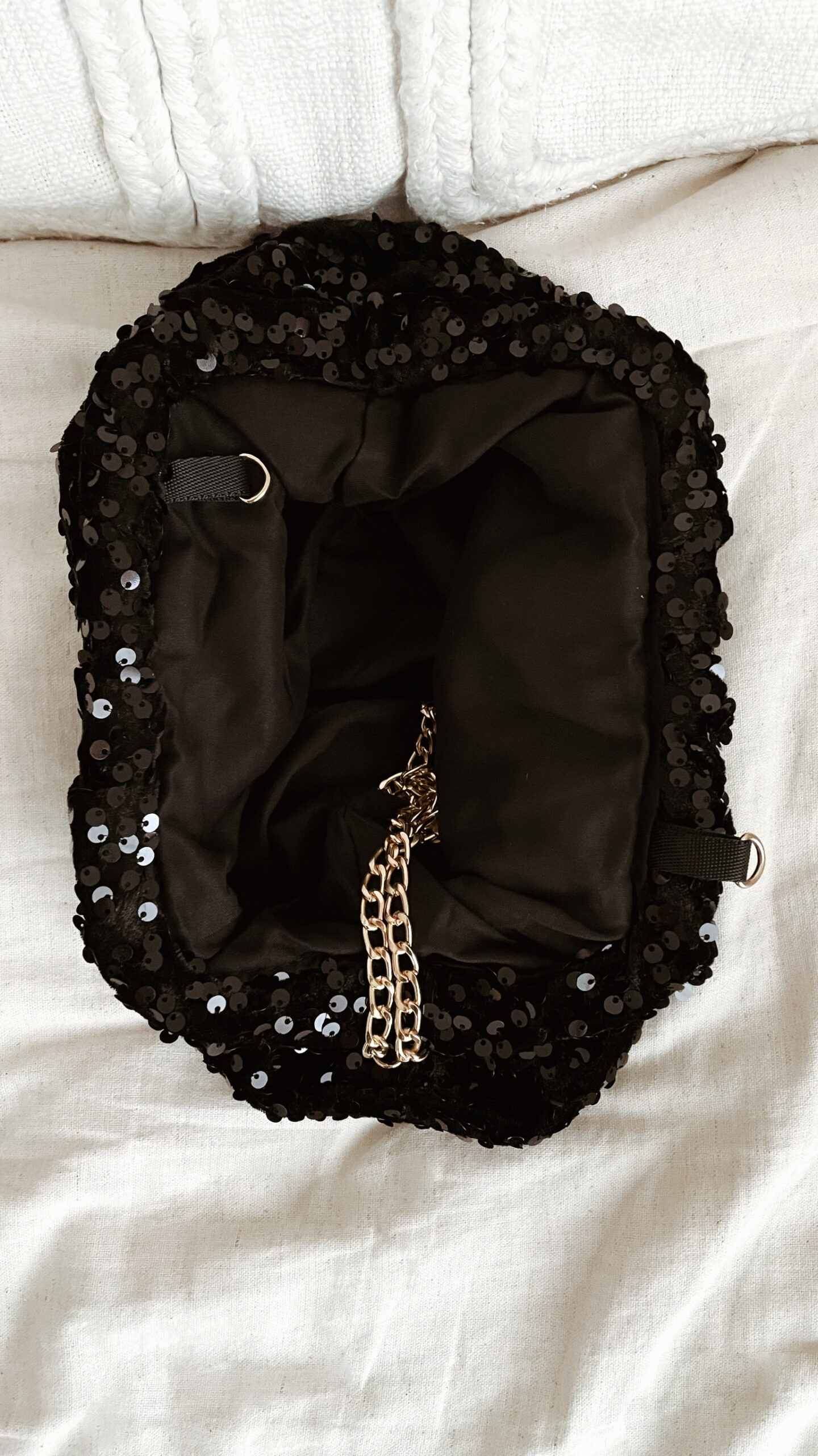 Femme tenant un sac à sequins noir scintillant, assorti à une tenue brune élégante avec chemisier et blazer en laine.
