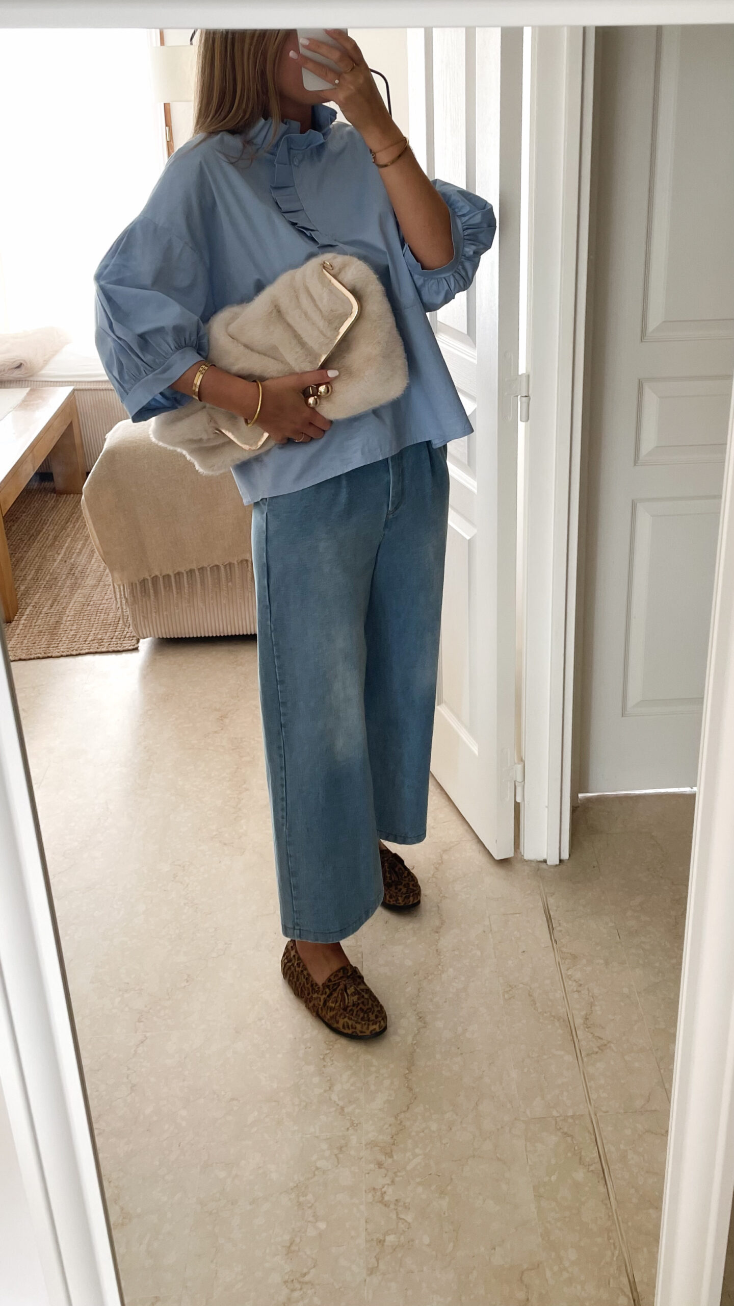 une femme qui porte une blouse Celine volantée bleue avec le jean bleu gabriel et le sac fourrure ecru