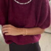 Femme portant un pull en maille bordeaux orné de strass au col, associé à une jupe noire courte et des bijoux dorés.