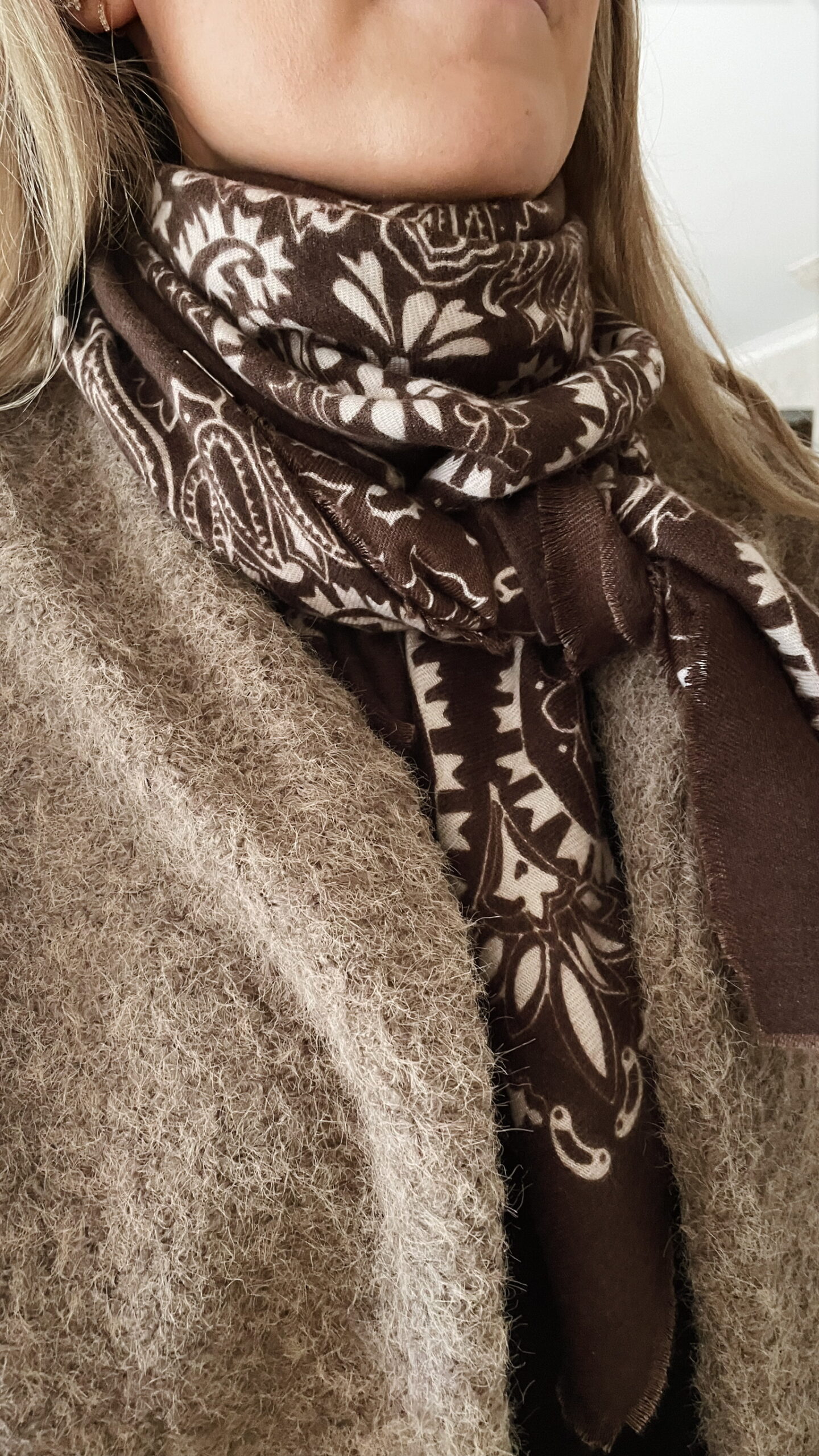 Écharpe femme marron et beige à motifs floraux nouée élégamment autour du cou, assortie à un gilet en laine texturée.