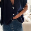 Femme portant une chemise oversize bleu clair à volants et un jean bleu orné de strass sur les côtés, dans un intérieur lumineux et minimaliste.