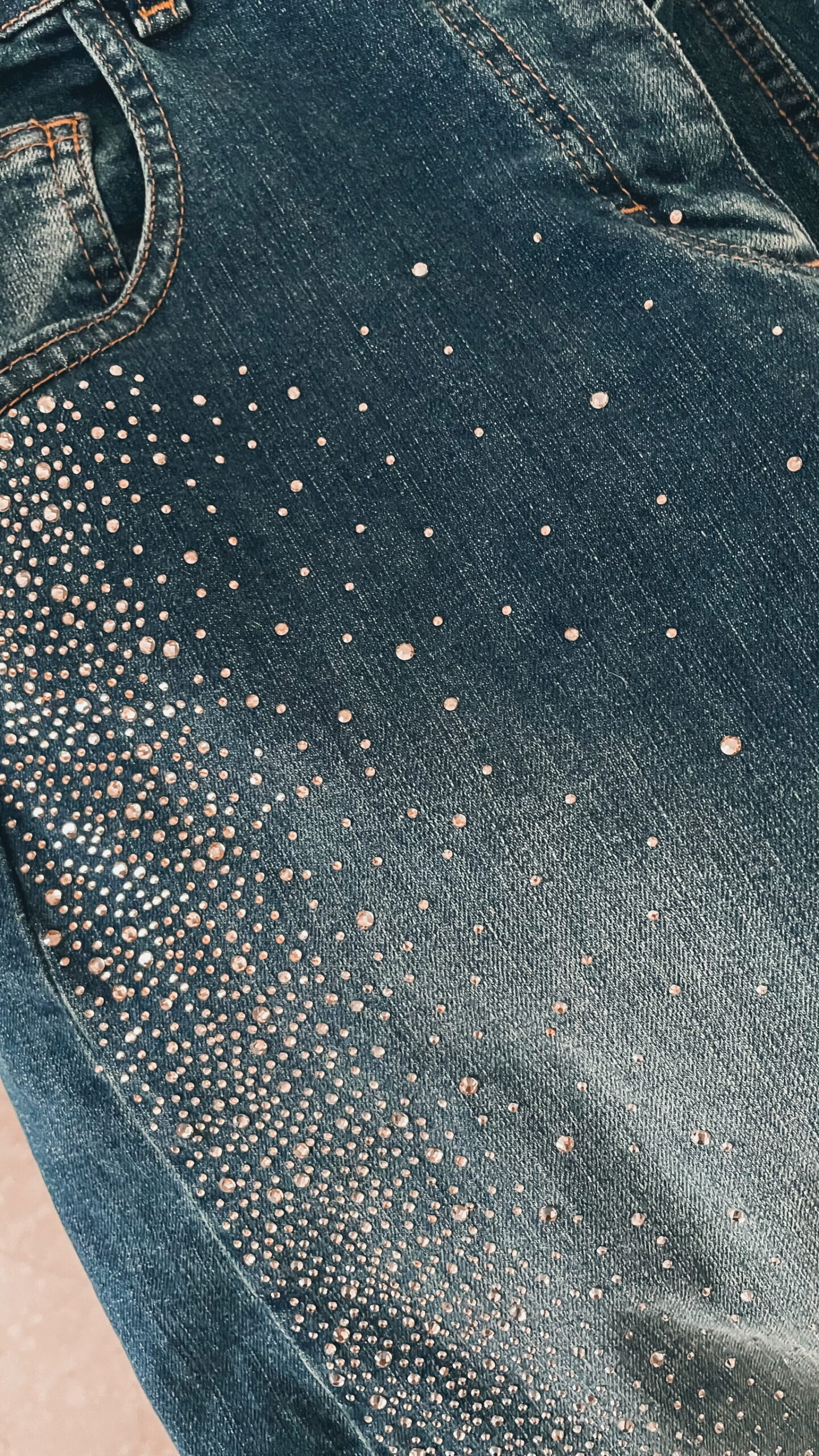 Femme portant une chemise oversize bleu clair à volants et un jean bleu orné de strass sur les côtés, dans un intérieur lumineux et minimaliste.