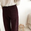 Femme portant un pantalon ballon en velours bordeaux, une blouse blanche à dentelle et un foulard imprimé beige, complété par des mocassins marron à boucle dorée.