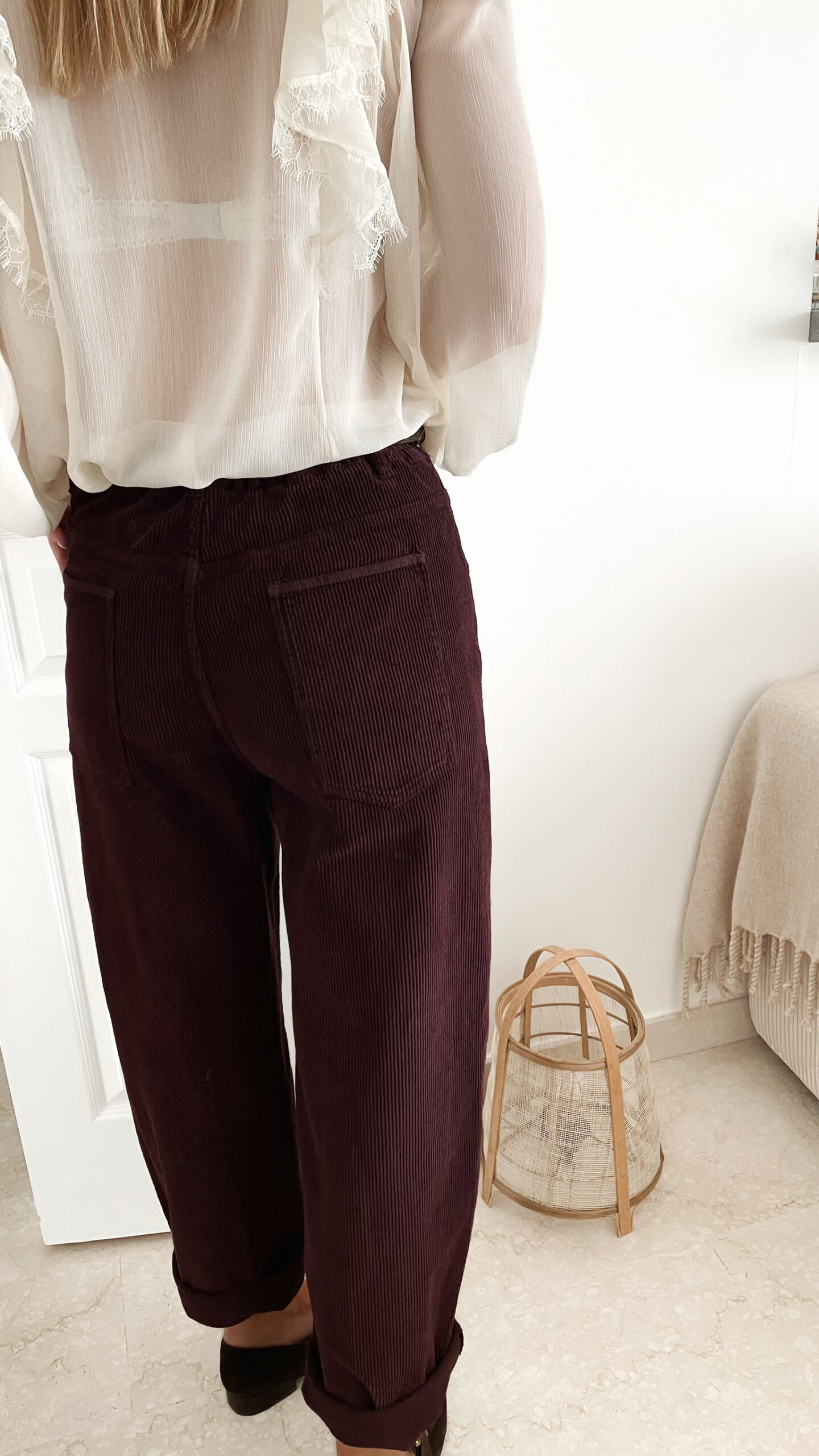 Femme portant un pantalon ballon en velours bordeaux, une blouse blanche à dentelle et un foulard imprimé beige, complété par des mocassins marron à boucle dorée.