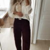 Femme portant un pantalon ballon en velours bordeaux, une blouse blanche à dentelle et un foulard imprimé beige, complété par des mocassins marron à boucle dorée.