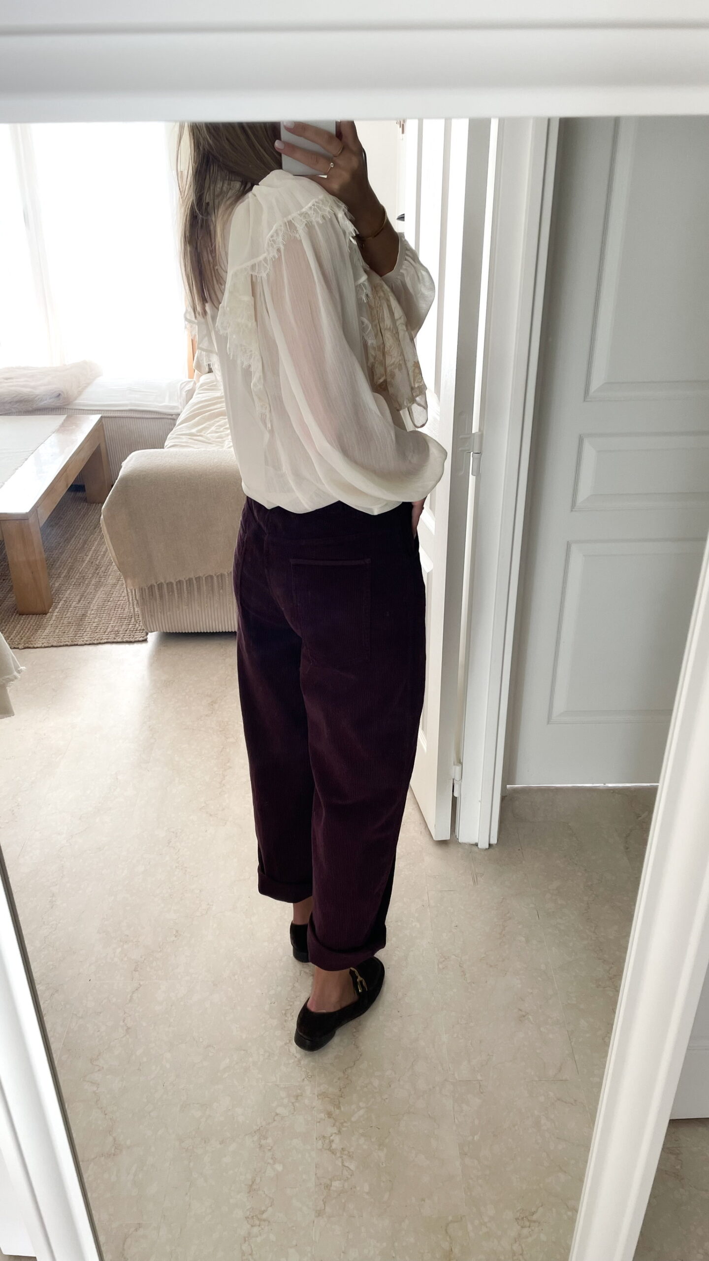 Femme portant un pantalon ballon en velours bordeaux, une blouse blanche à dentelle et un foulard imprimé beige, complété par des mocassins marron à boucle dorée.