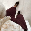 Femme portant un pantalon ballon en velours bordeaux, une blouse blanche à dentelle et un foulard imprimé beige, complété par des mocassins marron à boucle dorée.