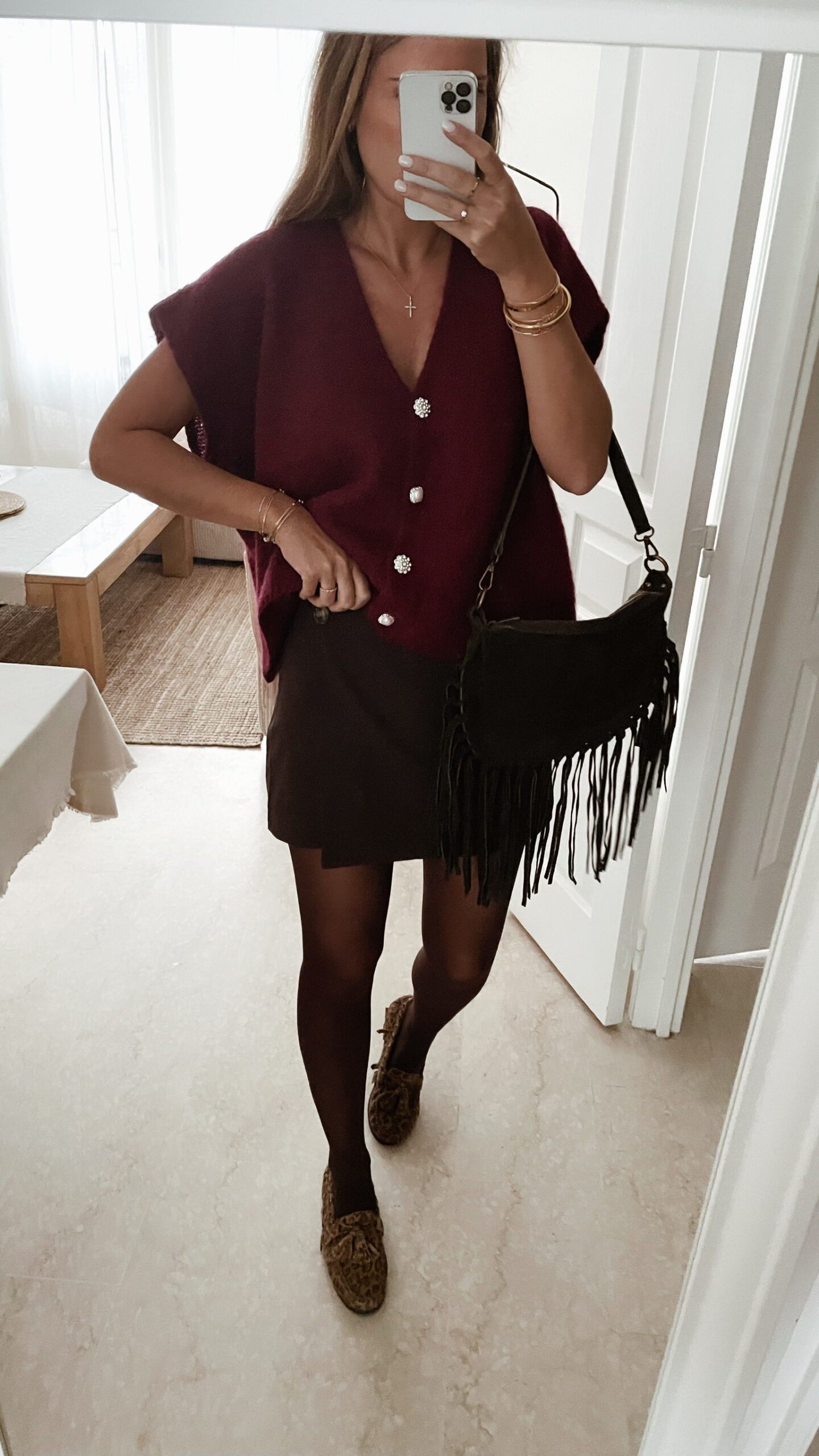 Femme portant un pull en mohair bordeaux à manches courtes, orné de boutons strass, associé à un foulard beige à motifs et des bijoux dorés au poignet.