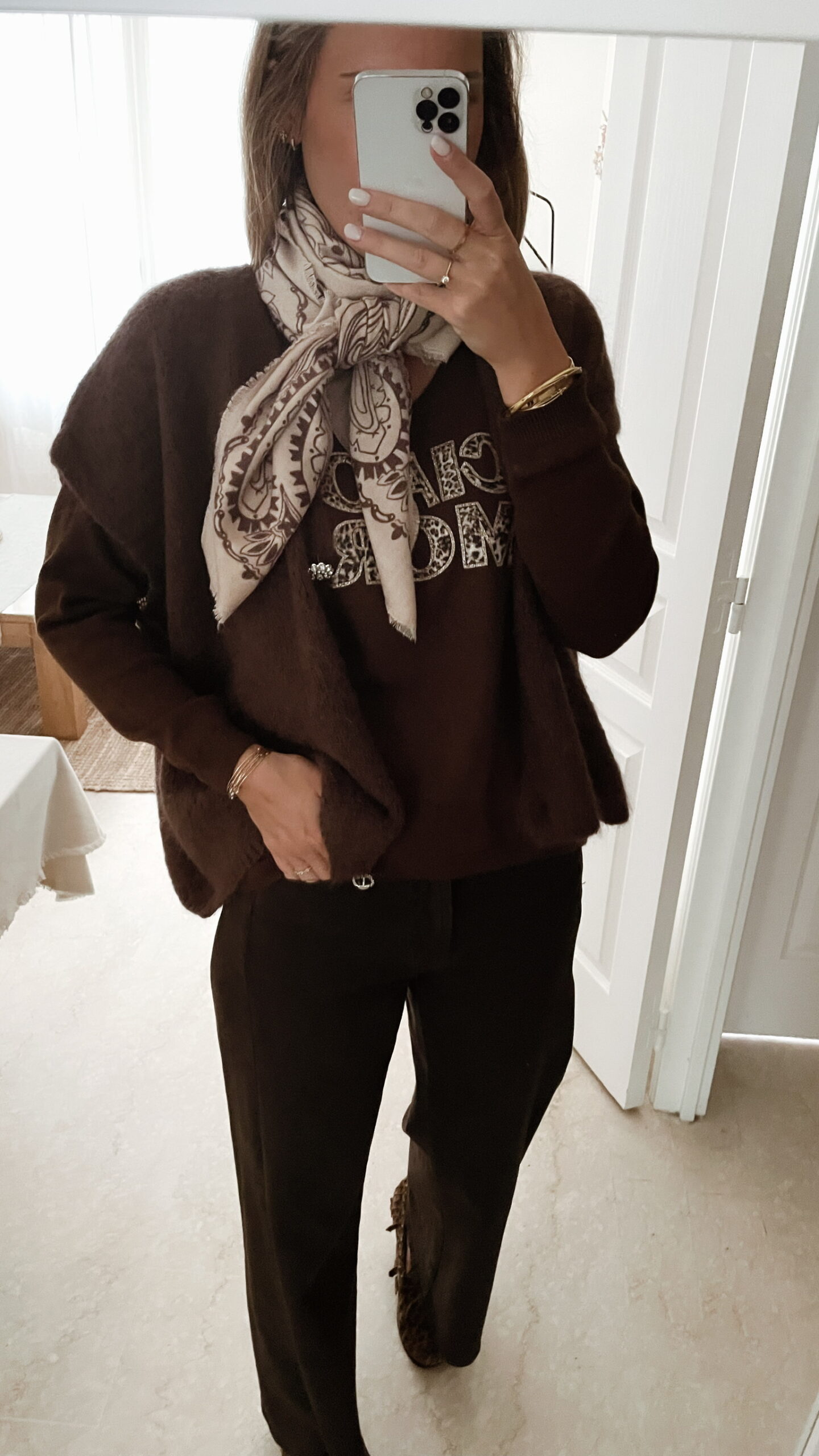 Femme portant un pull chocolat avec inscription « Ciao Amore », un gilet doux assorti, un pantalon marron foncé et un foulard beige et marron à motifs