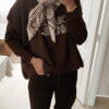 Femme portant un pull chocolat à inscription "Ciao Amore", associé à une écharpe imprimée beige et un pantalon foncé, pour un look automnal chic et décontracté.