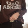 Femme portant un pull chocolat à inscription "Ciao Amore", associé à une écharpe imprimée beige et un pantalon foncé, pour un look automnal chic et décontracté.