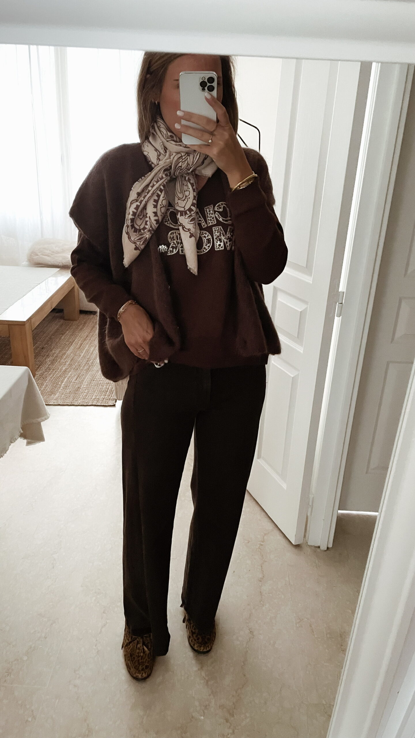 Femme portant un pull chocolat à inscription "Ciao Amore", associé à une écharpe imprimée beige et un pantalon foncé, pour un look automnal chic et décontracté.