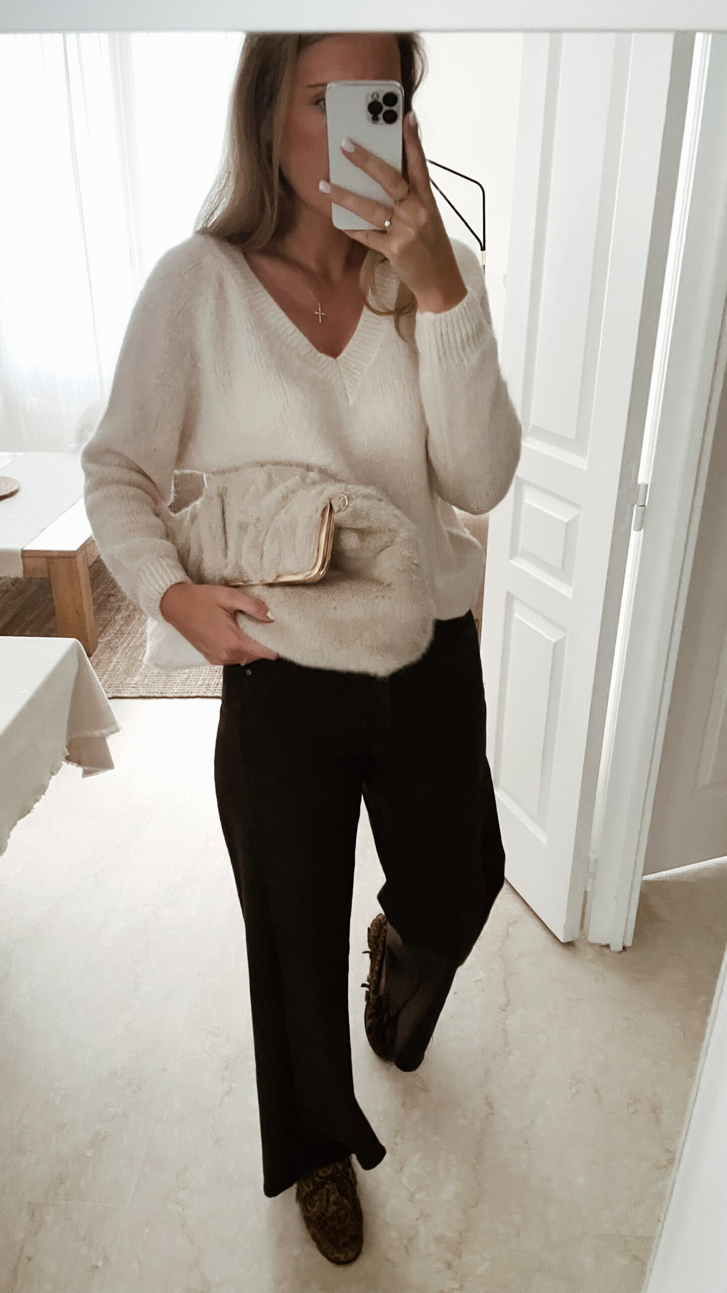 Femme portant un pull doux en alpaga couleur ecru, associé à un pantalon marron foncé à jambe large, une ceinture fine dorée, et des mocassins imprimés léopard.