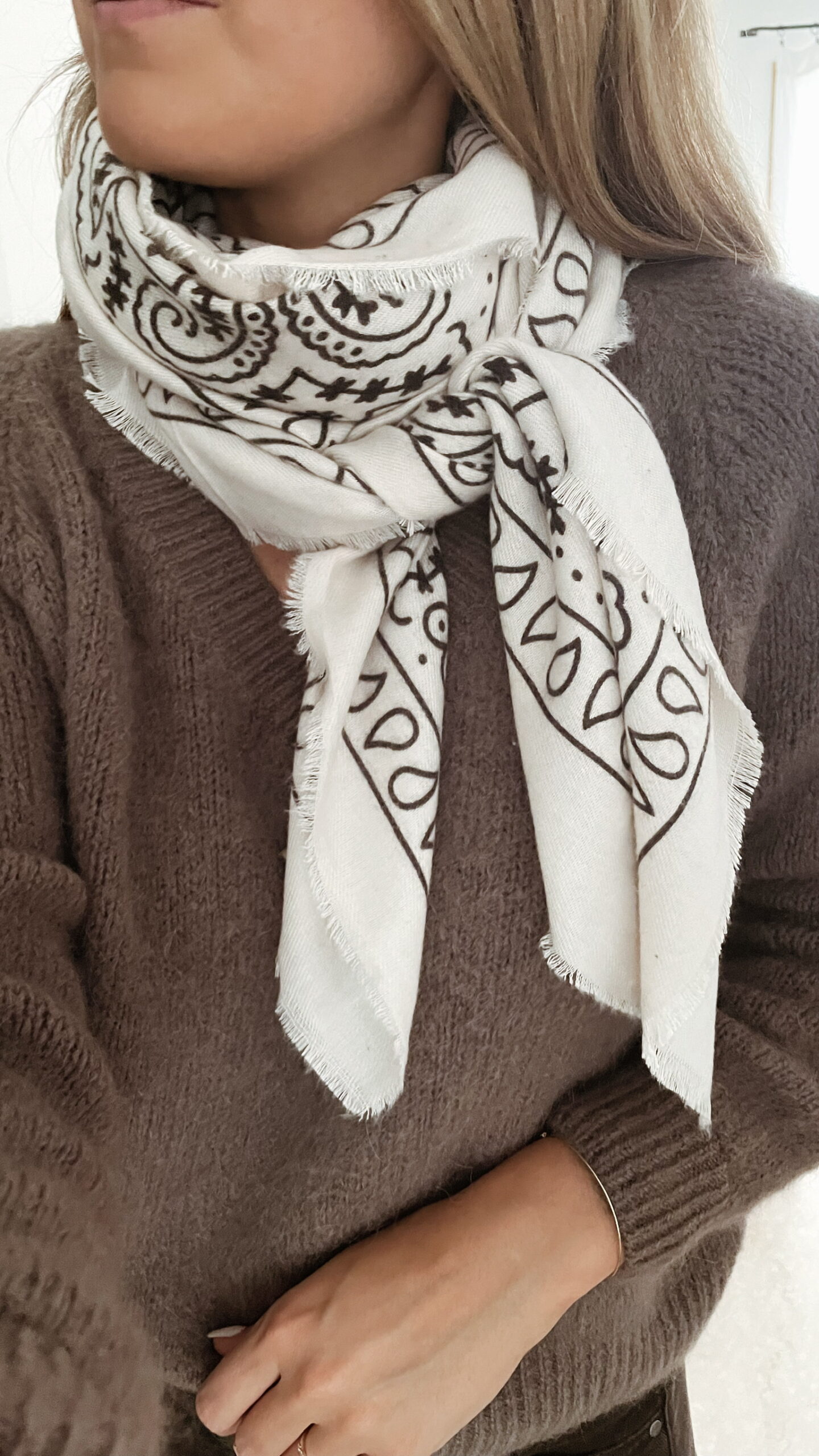 Femme portant un pull doux en alpaga couleur taupe, associé à un pantalon foncé à jambe large, une ceinture fine dorée, un foulard beige à motifs et des mocassins imprimés léopard.