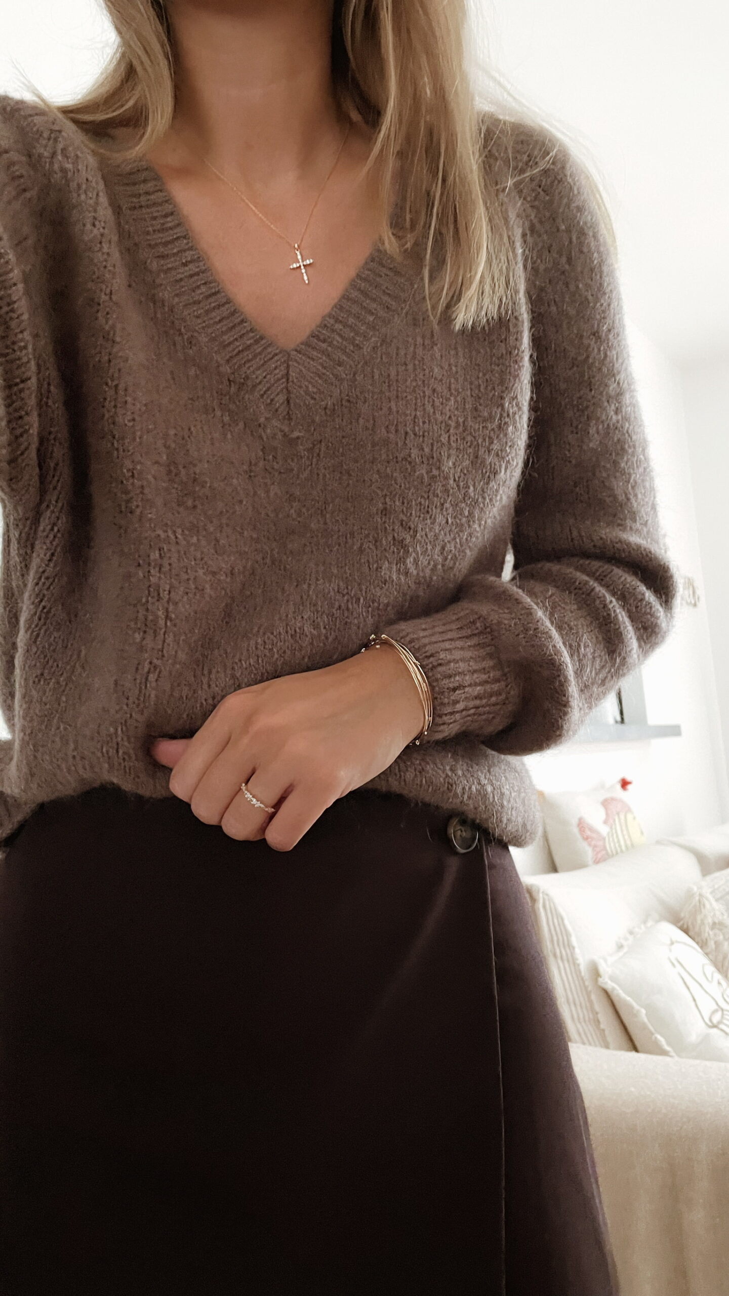 Femme portant un pull doux en alpaga couleur taupe, associé à un pantalon foncé à jambe large, une ceinture fine dorée, un foulard beige à motifs et des mocassins imprimés léopard.