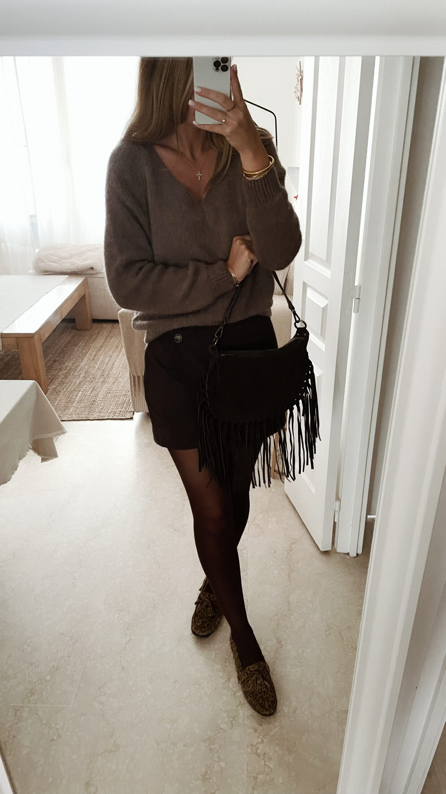 Femme portant un pull doux en alpaga couleur taupe, associé à un pantalon foncé à jambe large, une ceinture fine dorée, un foulard beige à motifs et des mocassins imprimés léopard.