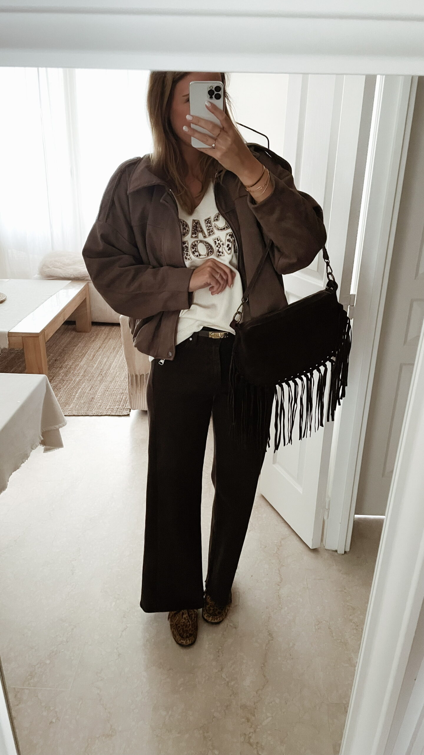 Femme portant un pull écru “Ciao Amore” avec un pantalon foncé, une veste en daim taupe et un sac à franges, pour un look automnal élégant et décontracté.