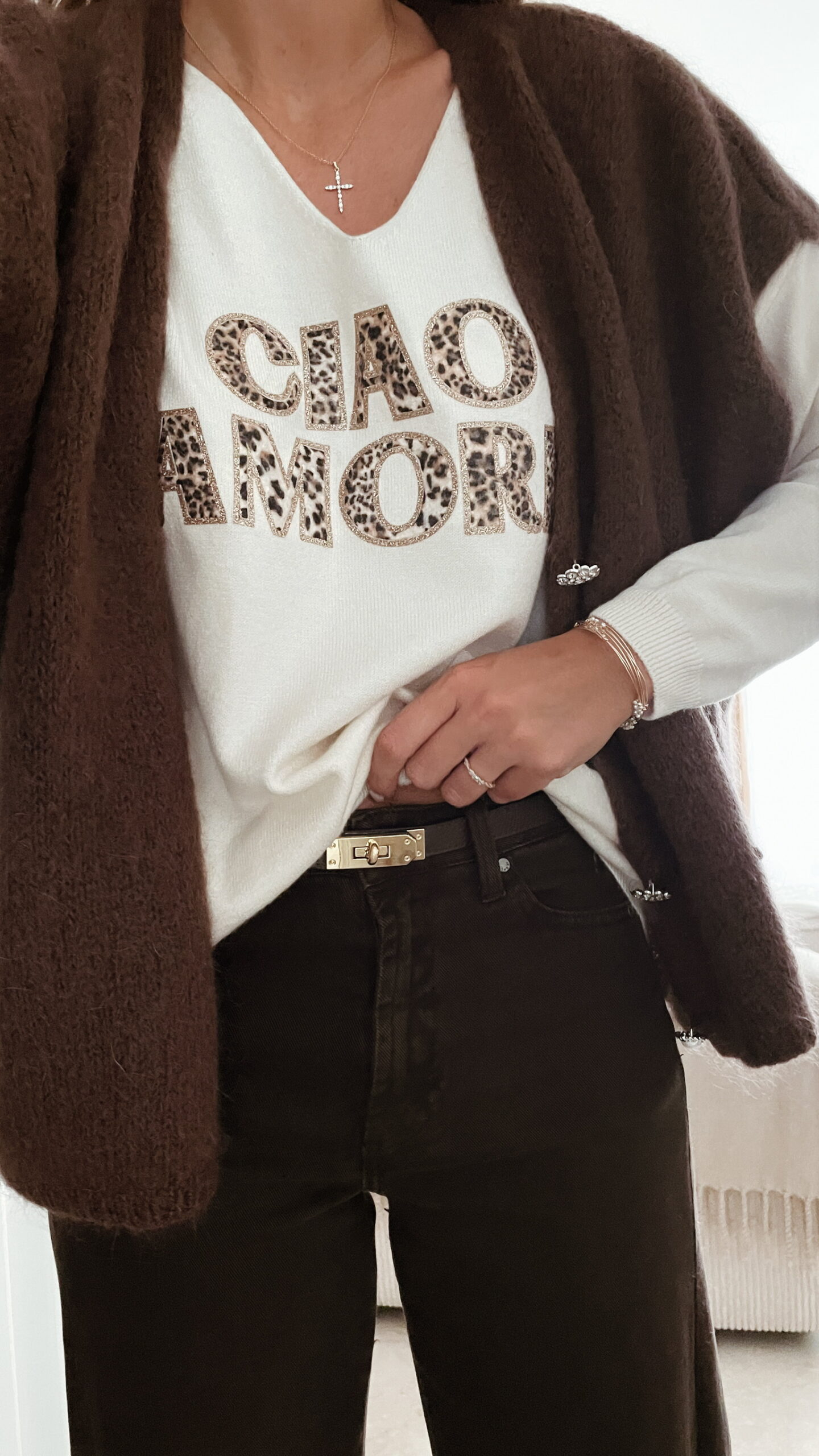 Femme portant un pull écru “Ciao Amore” avec un pantalon foncé, une veste en daim taupe et un sac à franges, pour un look automnal élégant et décontracté.