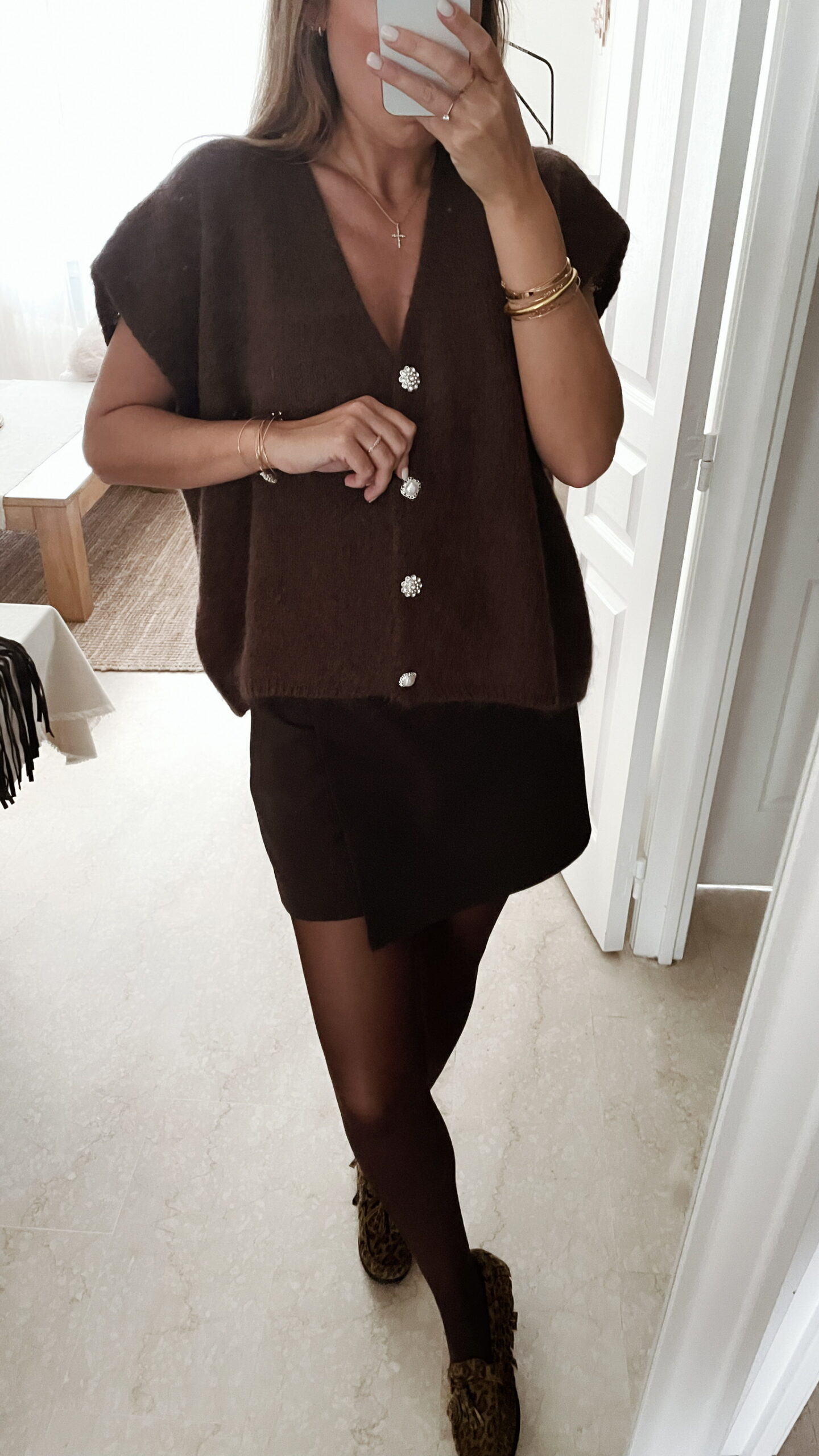 Femme portant un pull en mohair marron à manches courtes, orné de boutons strass, assorti à un sac en daim marron à franges et des bijoux dorés.