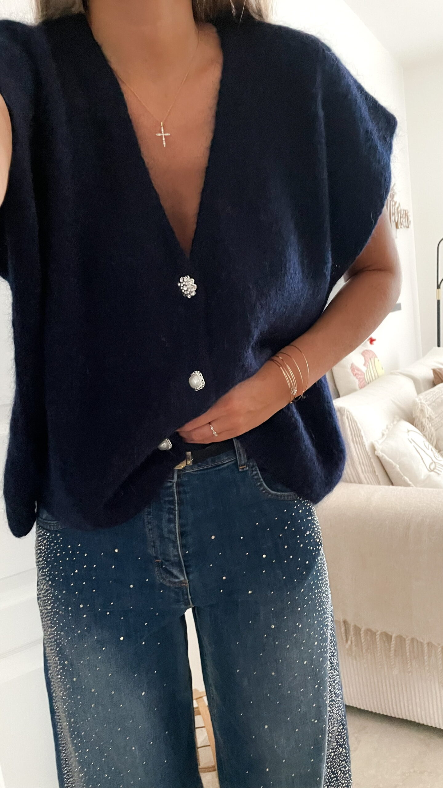 Femme portant un pull bleu en mohair à boutons bijoux et un pantalon en jean bleu foncé orné de strass, photographiée dans un intérieur lumineux.