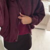 Femme portant une veste effet daim couleur bordeaux, assortie à un pull ton sur ton, une jupe noire et des collants foncés, dans un intérieur lumineux.