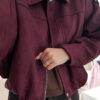 Femme portant une veste effet daim couleur bordeaux, assortie à un pull ton sur ton, une jupe noire et des collants foncés, dans un intérieur lumineux.
