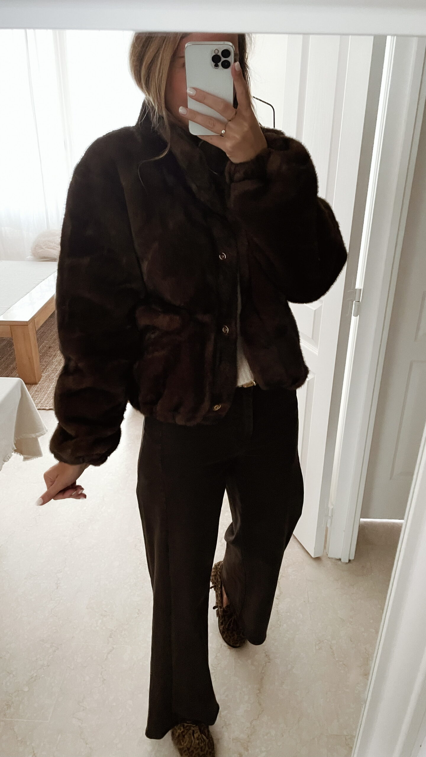 Femme portant une veste en fausse fourrure marron à col montant, associée à un pantalon foncé et des mocassins imprimés léopard.