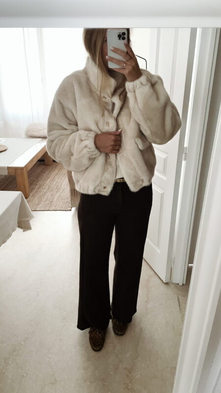 Femme portant une veste en fausse fourrure écrue à col montant, associée à un pantalon foncé et des mocassins imprimés léopard.