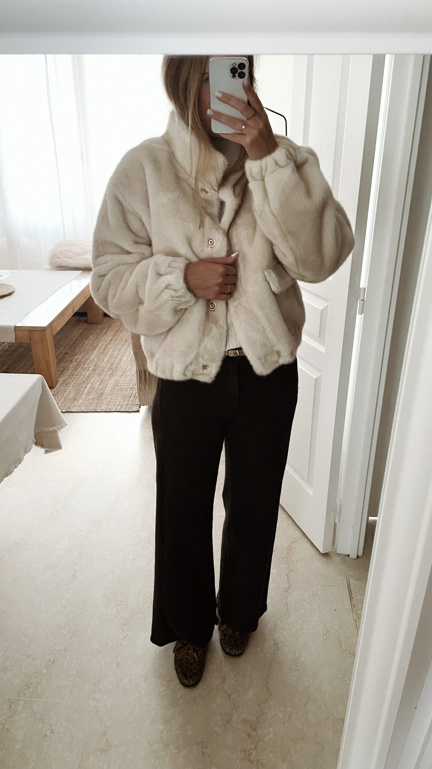 Femme portant une veste en fausse fourrure écrue à col montant, associée à un pantalon foncé et des mocassins imprimés léopard.