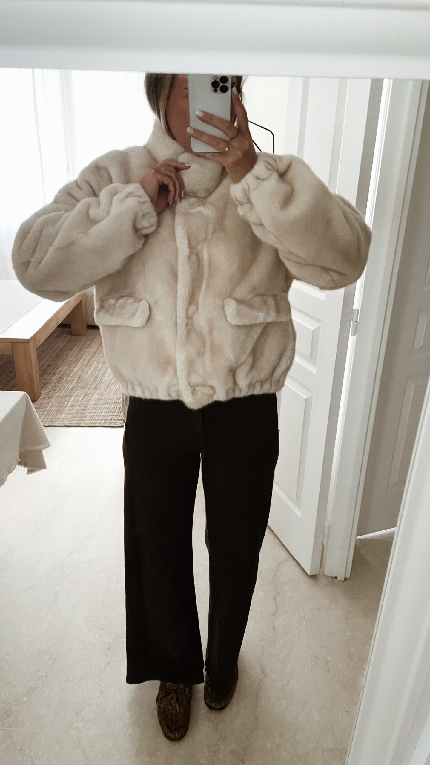 Femme portant une veste en fausse fourrure écrue à col montant, associée à un pantalon foncé et des mocassins imprimés léopard.