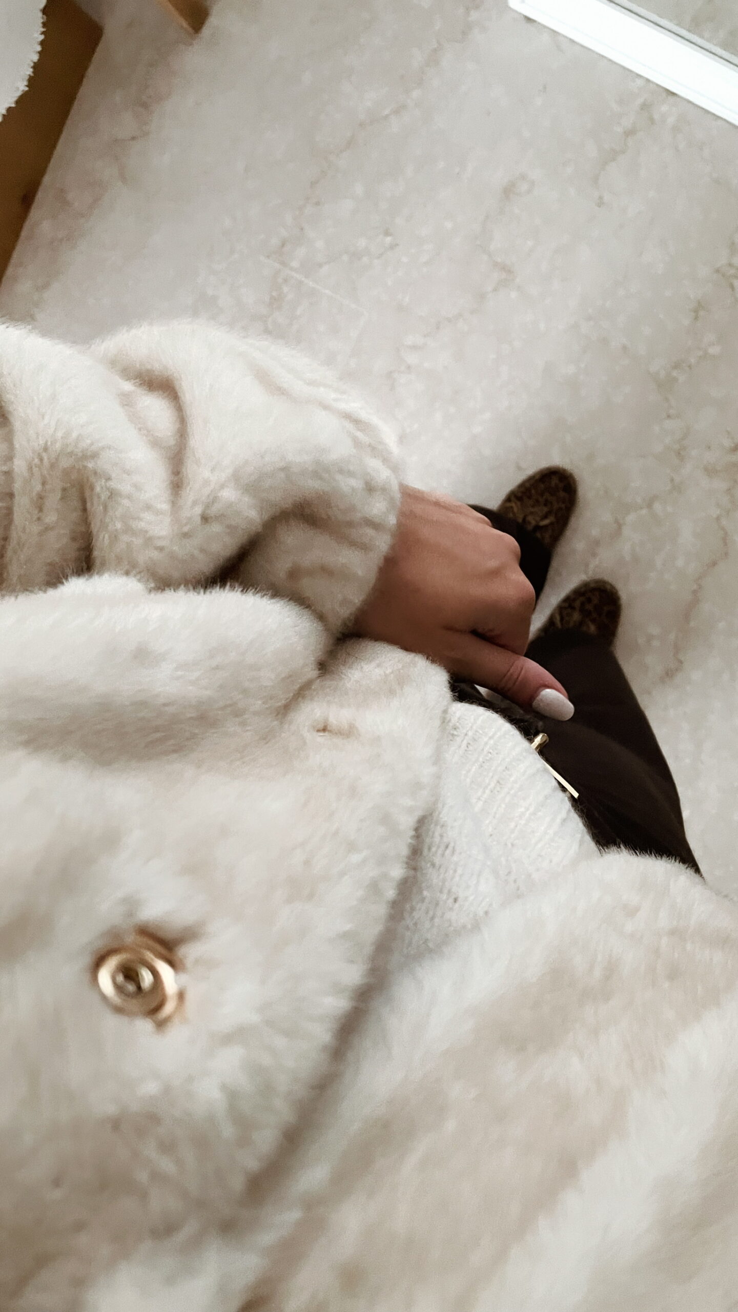 Femme portant une veste en fausse fourrure écrue à col montant, associée à un pantalon foncé et des mocassins imprimés léopard.