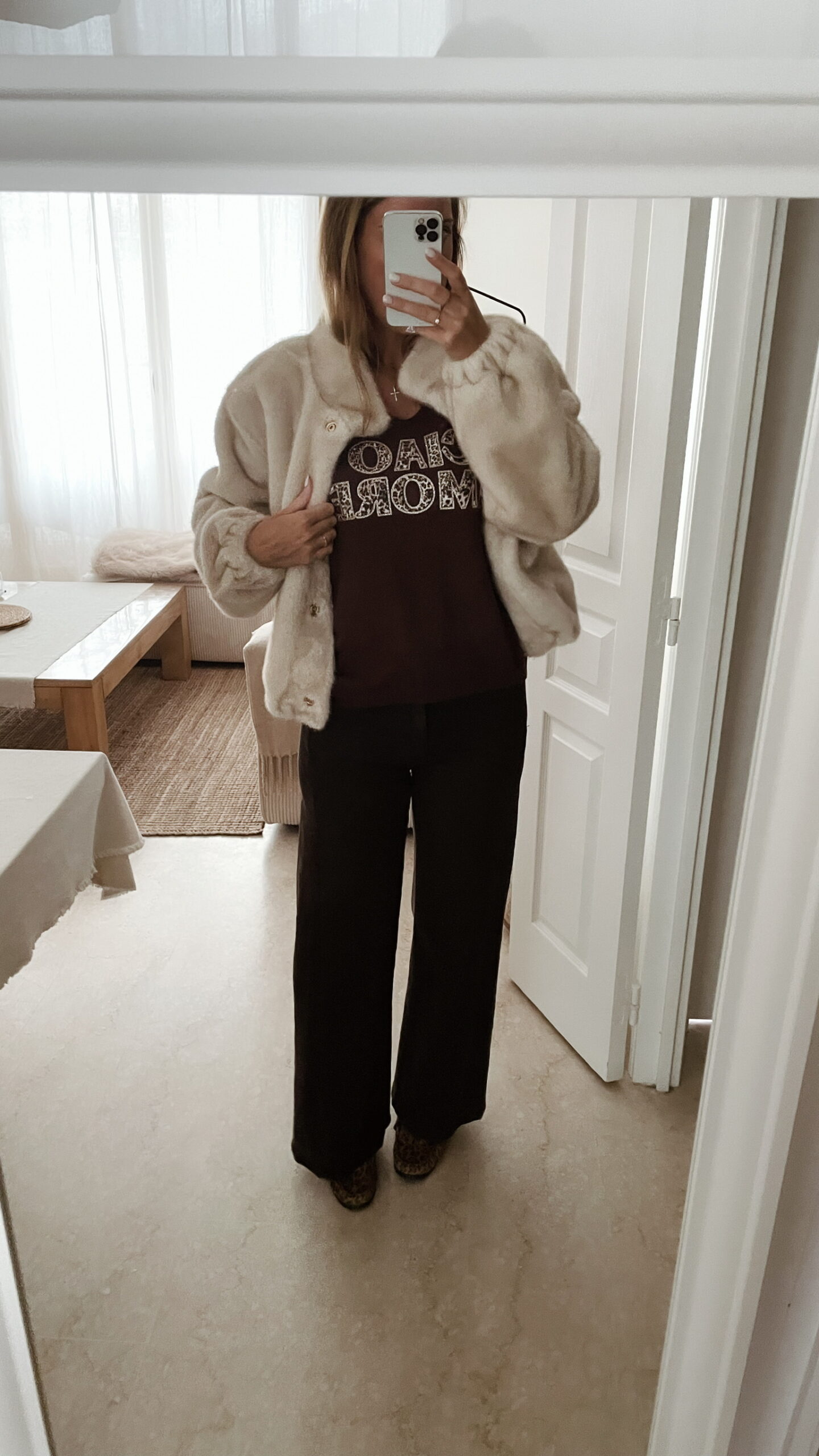 Femme portant une veste en fausse fourrure écrue à col montant, associée à un pantalon foncé et des mocassins imprimés léopard.