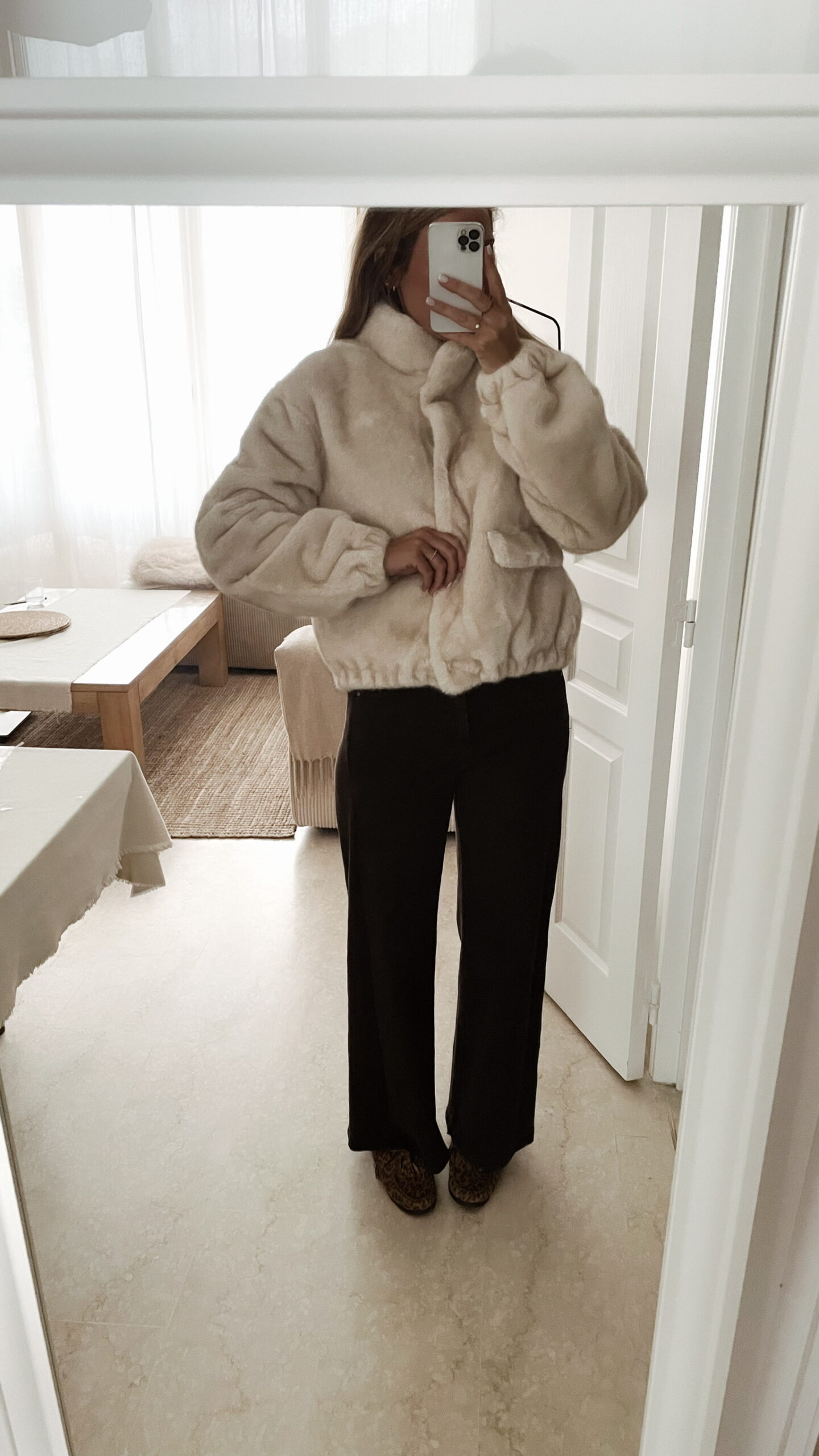 Femme portant une veste en fausse fourrure écrue à col montant, associée à un pantalon foncé et des mocassins imprimés léopard.