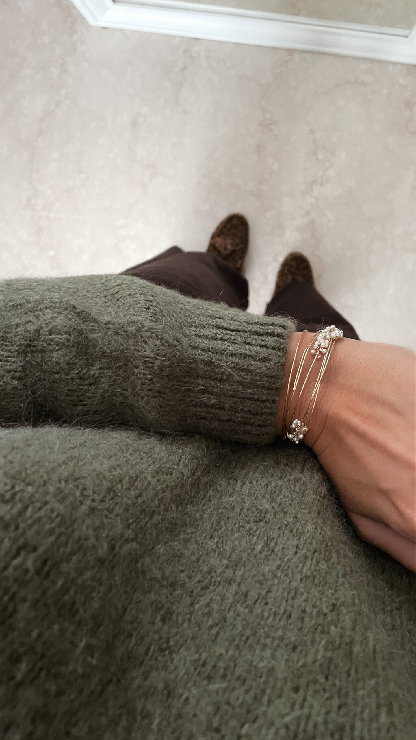 Femme portant un pull doux en alpaga couleur kaki, associé à un pantalon marron foncé à jambe large, une ceinture fine dorée, et des mocassins imprimés léopard.