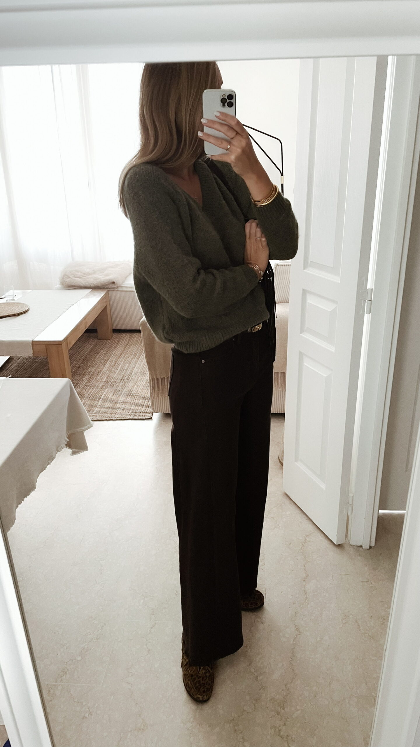 Femme portant un pull doux en alpaga couleur kaki, associé à un pantalon marron foncé à jambe large, une ceinture fine dorée, et des mocassins imprimés léopard.