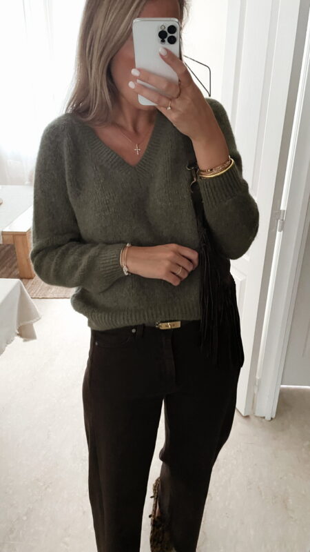Femme portant un pull doux en alpaga couleur kaki, associé à un pantalon marron foncé à jambe large, une ceinture fine dorée, et des mocassins imprimés léopard.