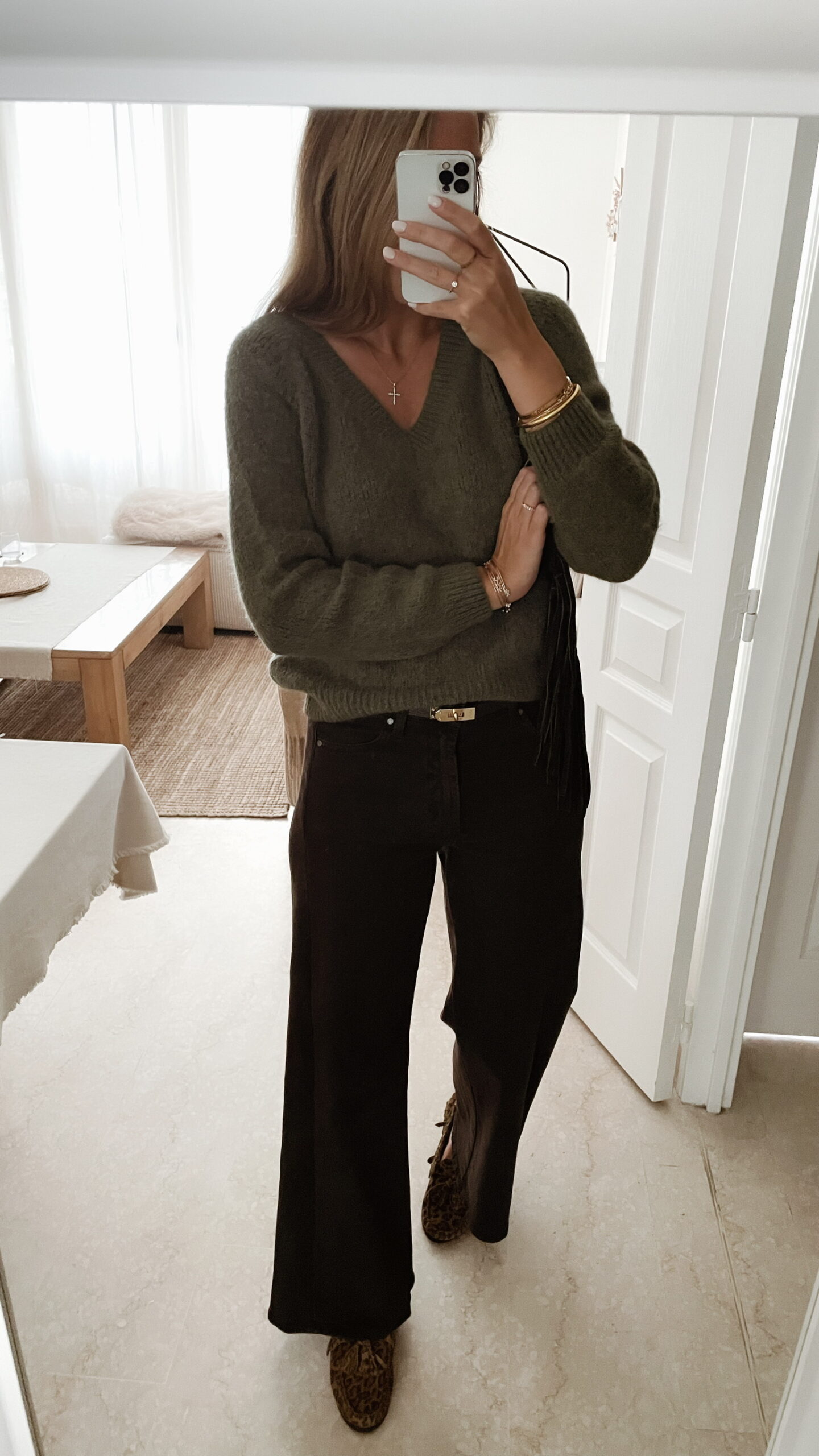 Femme portant un pull doux en alpaga couleur kaki, associé à un pantalon marron foncé à jambe large, une ceinture fine dorée, et des mocassins imprimés léopard.