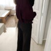 Femme portant une veste effet daim couleur bordeaux, assortie à un pull ton sur ton, une jupe noire et des collants foncés, dans un intérieur lumineux.