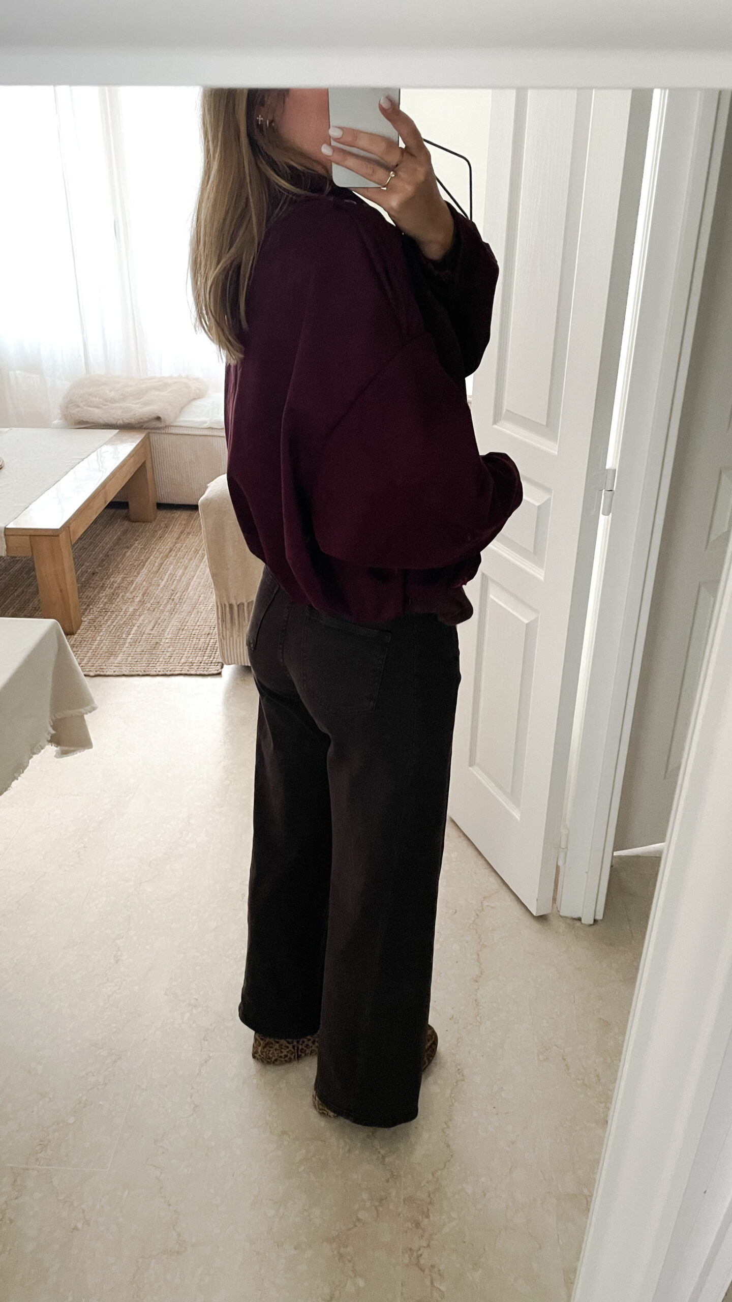 Femme portant une veste effet daim couleur bordeaux, assortie à un pull ton sur ton, une jupe noire et des collants foncés, dans un intérieur lumineux.