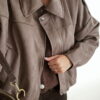 Femme portant une veste effet daim couleur marron taupe, assortie à un pull en alpaga taupe ton sur ton, un pantalon marron, une echarpe à motifs et un sac en daim marron avec des franges dans un intérieur lumineux.