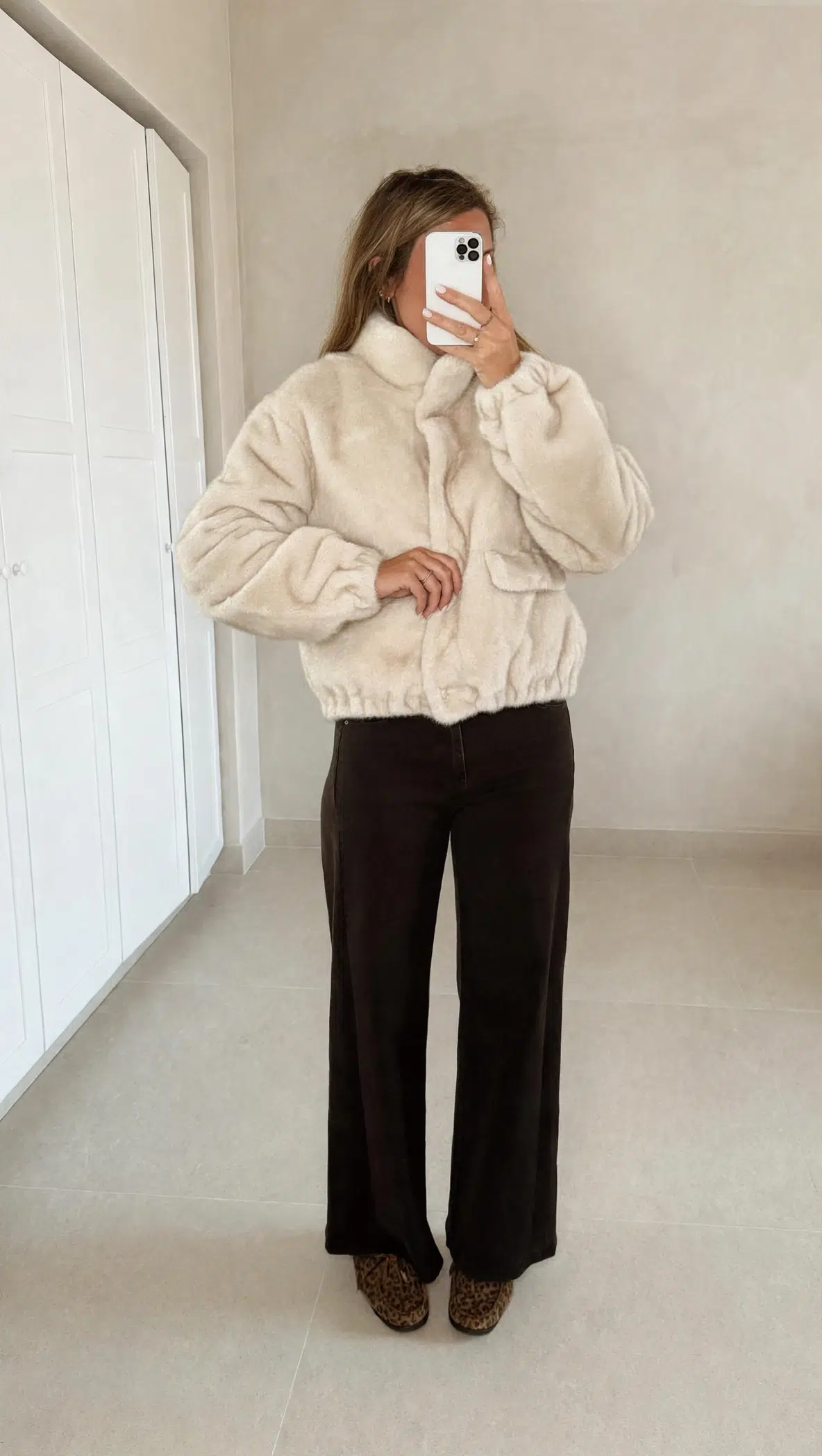 Femme portant une veste en fausse fourrure écrue à col montant, associée à un pantalon foncé et des mocassins imprimés léopard.