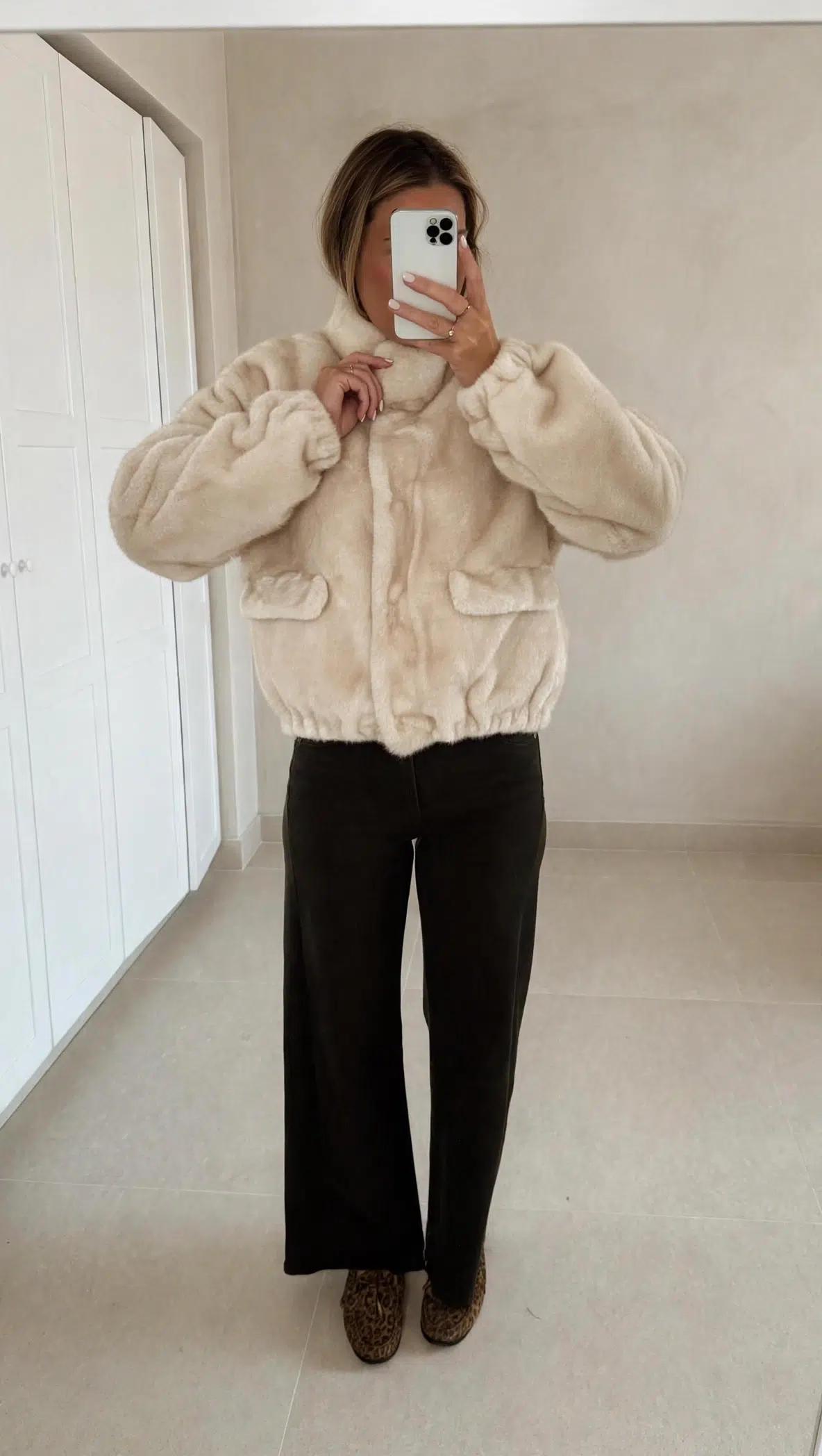 Femme portant une veste en fausse fourrure écrue à col montant, associée à un pantalon foncé et des mocassins imprimés léopard.