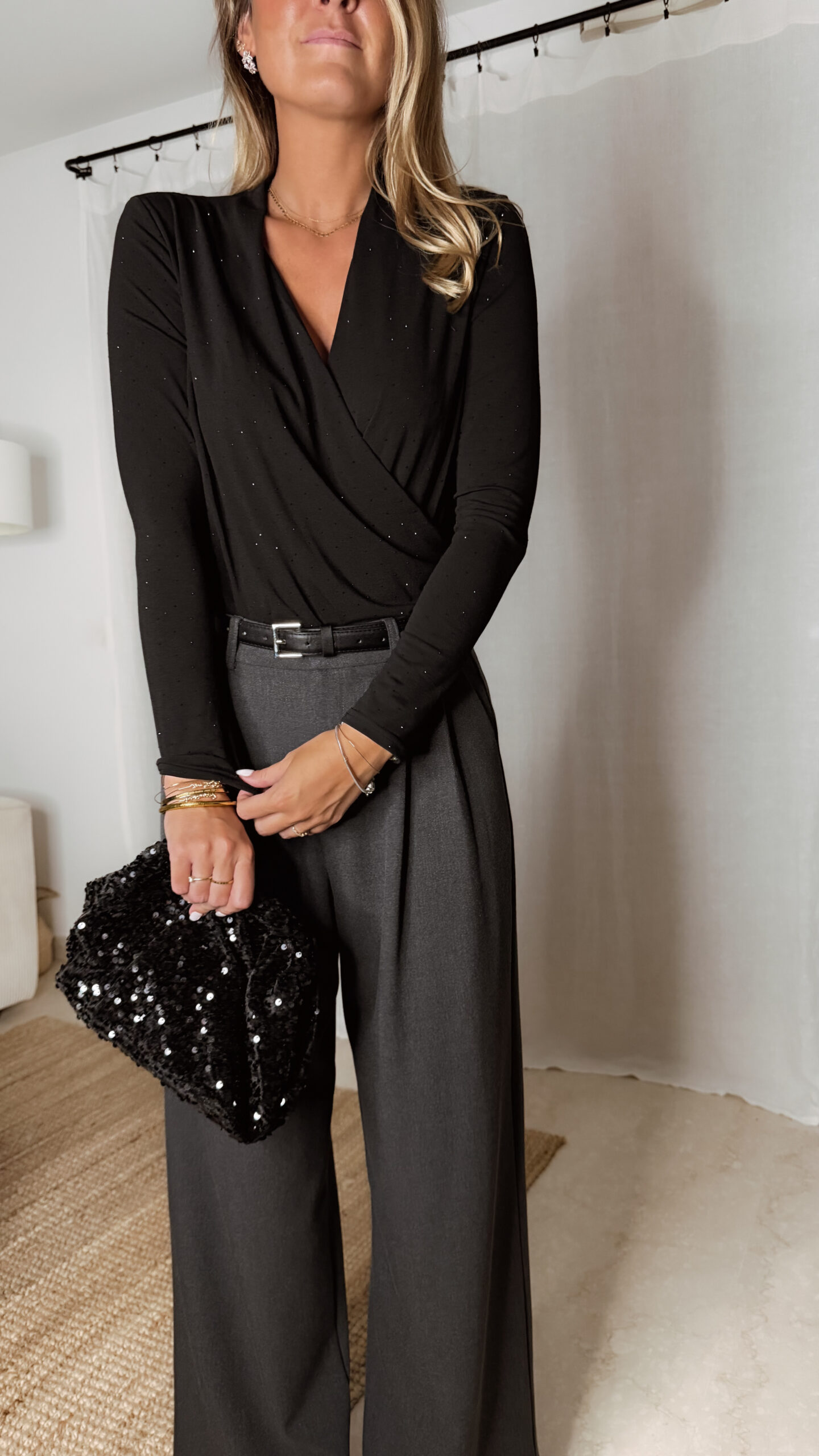 « Femme portant un body noir à strass avec un pantalon large gris et une pochette noire pailletée, tenue élégante de soirée. »