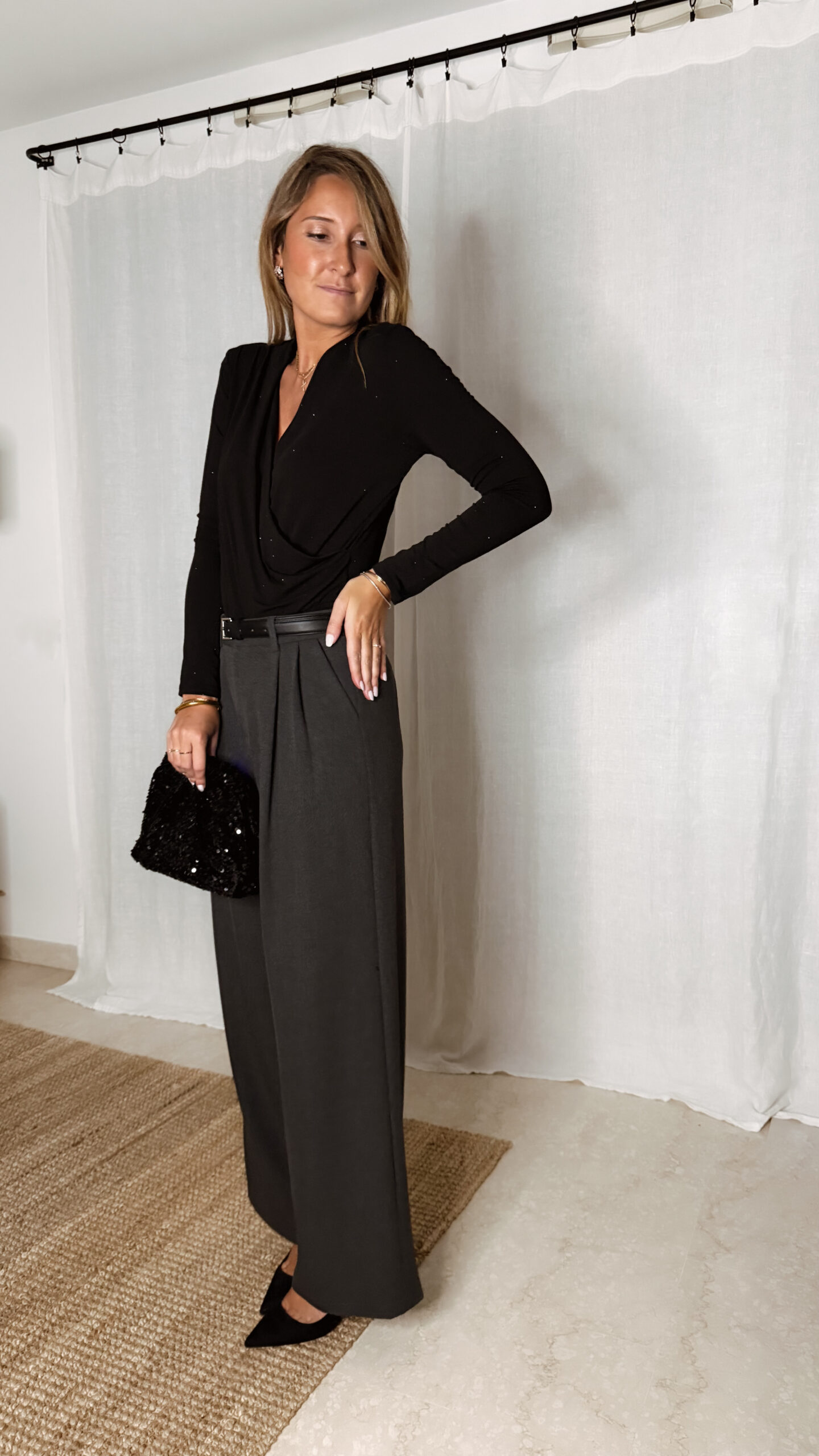 « Femme portant un body noir à strass avec un pantalon large gris et une pochette noire pailletée, tenue élégante de soirée. »