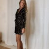 Femme portant une combinaison short à sequins noirs et argentés, manches longues et décolleté croisé.