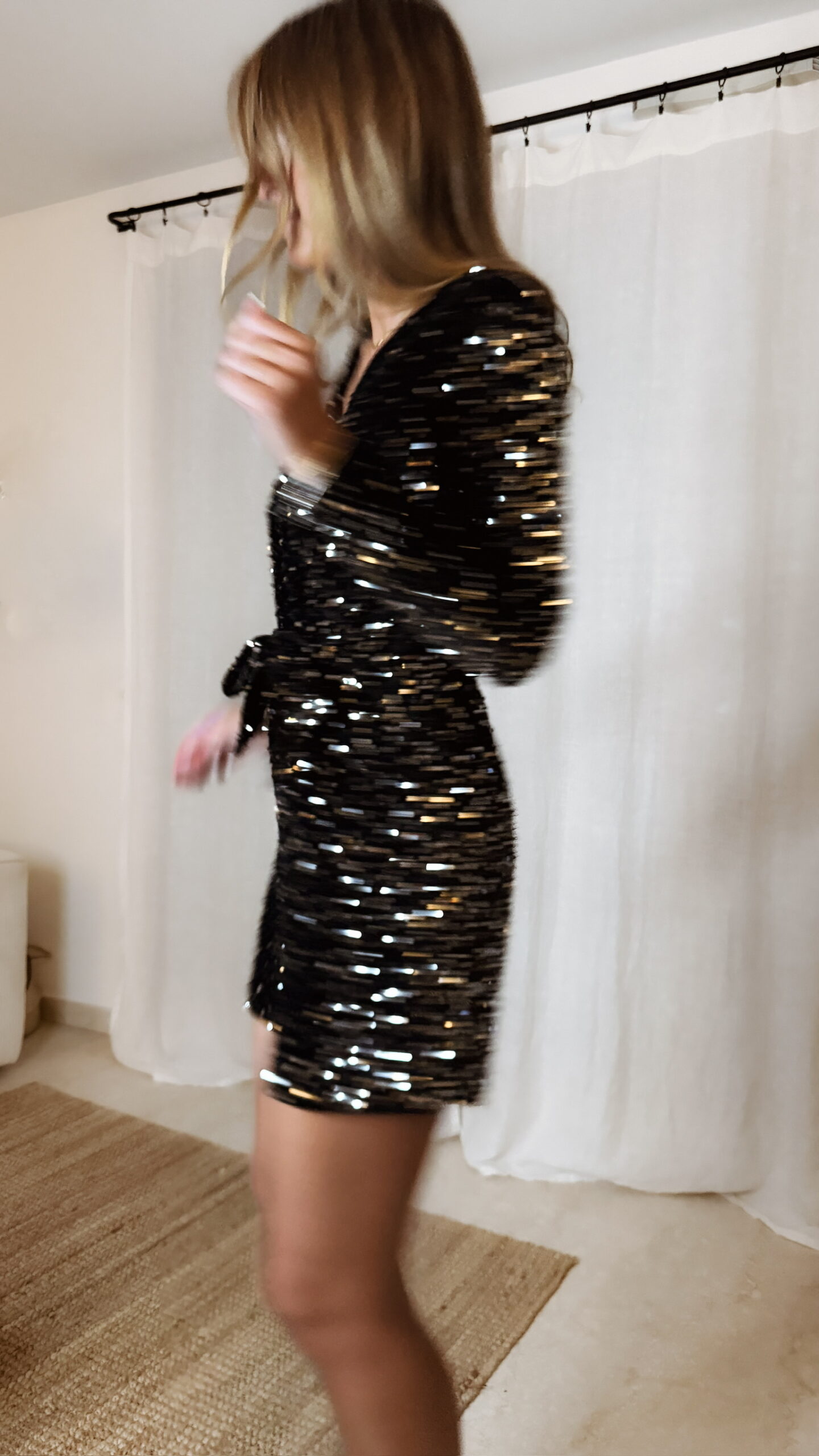 Femme portant une combinaison short à sequins noirs et argentés, manches longues et décolleté croisé.