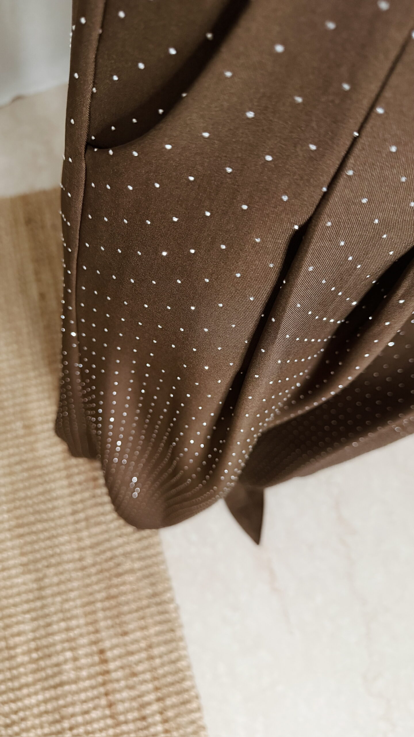 Femme portant un top en satin marron avec dentelle et un pantalon large marron à strass, accompagné d’une pochette brillante.