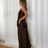 Femme portant un top en satin marron avec dentelle et un pantalon large marron à strass, accompagné d’une pochette brillante.