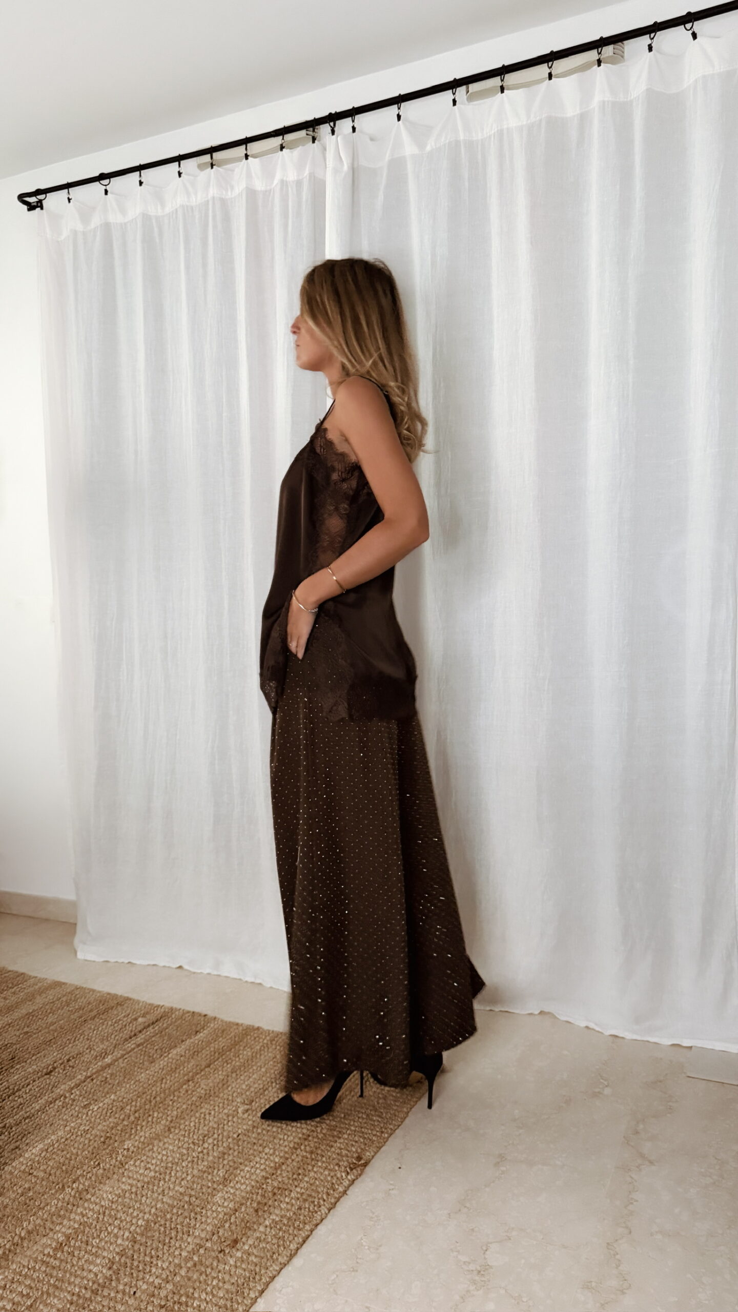 Femme portant un top en satin marron avec dentelle et un pantalon large marron à strass, accompagné d’une pochette brillante.